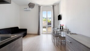 Une cuisine moderne avec un coin repas, un canapé noir et une vue à travers une porte vitrée.