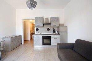 A modern kitchen with grey cabinets, a built-in oven, and a grey sofa in the living area.