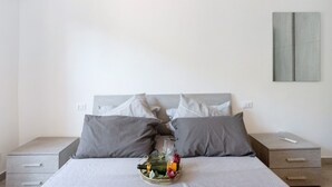 Un lit bien fait, avec des oreillers, une table de chevet sur laquelle se trouve une télécommande, et un plateau avec une bouteille et des verres posés sur le lit.