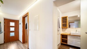 A hallway leading to a bathroom with a wooden door, a white wall, and a mirror above the sink. - Apartment "Unterortsgut" with Private Garden & Wi-Fi (Dorf Tirol)