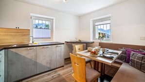 A modern kitchen with a dining area, wooden flooring, and a view of mountains through the windows. - Apartment "Unterortsgut" with Private Garden & Wi-Fi (Dorf Tirol)