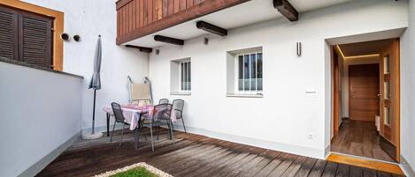 Un patio techado con una mesa y sillas, techo de madera y una puerta que da al interior.