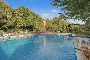 A swimming pool with clear blue water, surrounded by lush green trees and a building in the background.