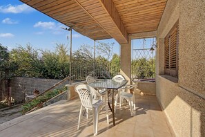 An outdoor patio with a table and chairs, a wooden ceiling, and a view of trees and a fence.
