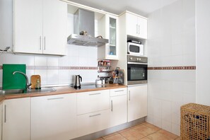 A kitchen with white cabinets, a microwave, an oven, a sink, and a wooden cutting board.