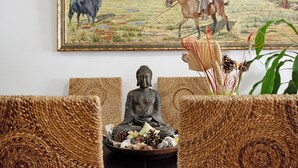 Una estàtua de Buda dins d'una safata amb ofrenes, una pintura d'una escena rural i una planta al primer pla.