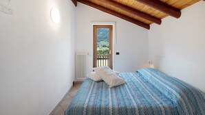 A bedroom with a wooden ceiling, a bed with patterned bedding, a white radiator, and a door leading to a balcony.