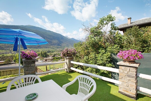 Une terrasse avec une table et des chaises, un parasol bleu et des pots de fleurs.