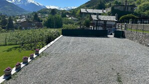 A building with a gravel driveway, a small garden with potted plants, and a mountainous backdrop.