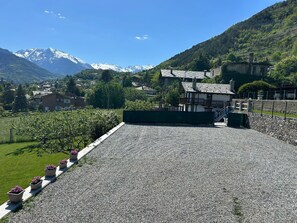 A building with a gravel driveway, a small garden with potted plants, and a mountainous backdrop.