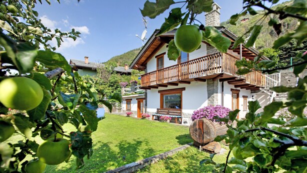 A house with a balcony, a lawn, and a mountain backdrop.