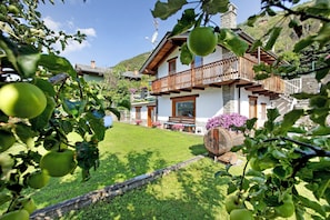 A house with a balcony, a lawn, and a mountain backdrop.