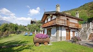 A two-story house with a balcony, a wooden barrel planter with flowers, and a staircase leading to the upper floor.