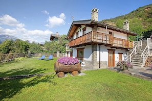 Una casa de dos pisos con un balcón, una jardinera de madera con flores y una escalera que conduce al piso superior.