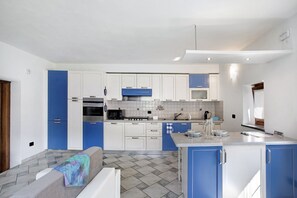 Una cocina moderna con armarios azul y blanco, una isla central y un rincón comedor con sofá.