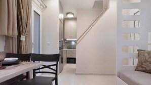 Una cocina moderna con armarios, una mesa de comedor con sillas, un sofá con un cojín estampado y una escalera.