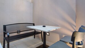 Zona d'estar a l'exterior amb una banca de metall, una taula i una cadira.