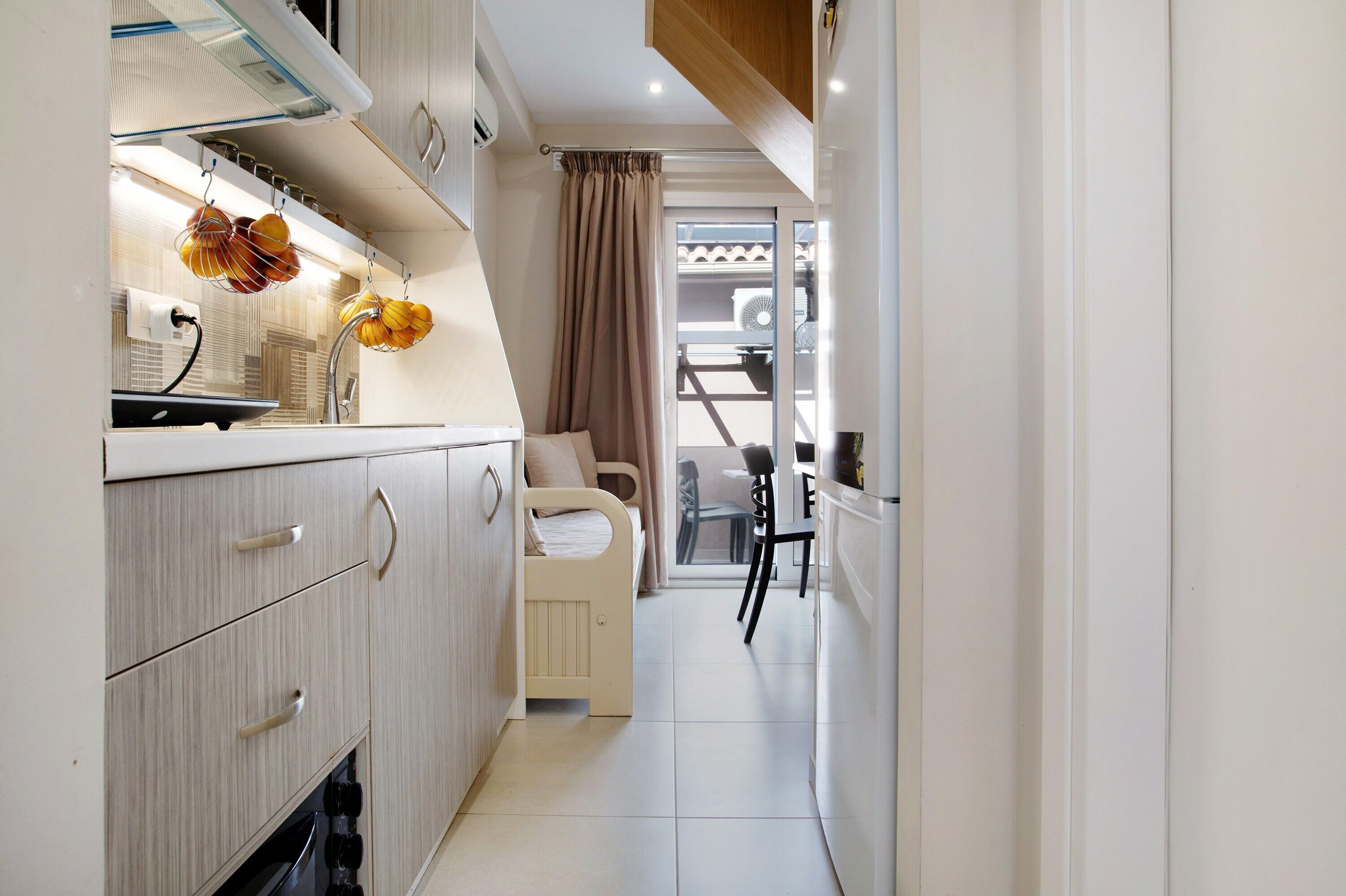 A narrow hallway with a kitchenette on one side, a child's bed in the center, and a dining area with chairs and a table at the end.