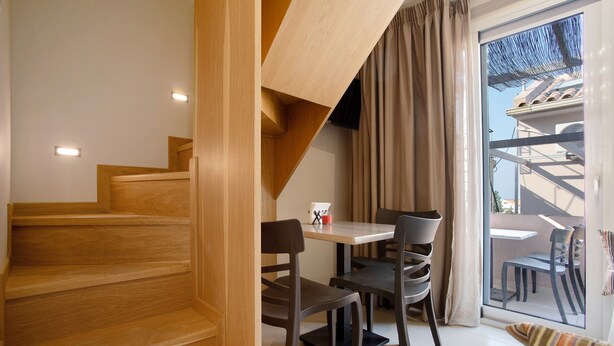 Un interior modern amb escala de fusta, zona de menjador amb caires i taula, i una porta corredissa de vidre que dona a un balcó exterior.
