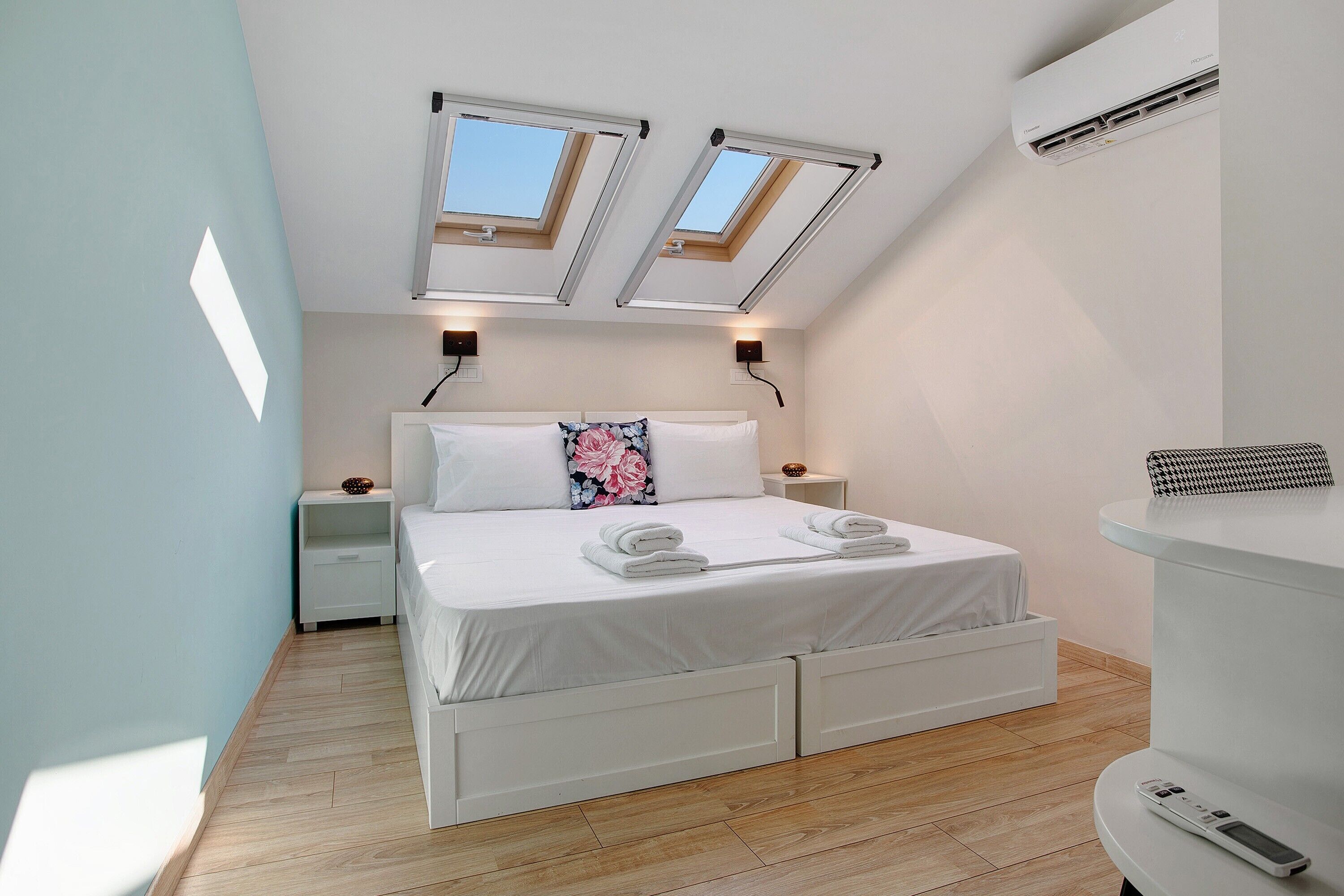 A bedroom with a bed, skylights, an air conditioner, a bedside table, and a nightstand.