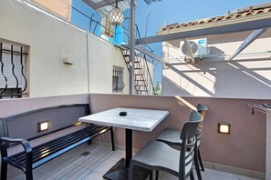 A balcony with a table, chairs, a bench, and a small wall-mounted light fixture.