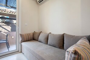A living room with a sofa, a striped pillow, a chair, and a sliding glass door leading to an outdoor area.