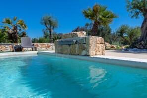 Ein Pool mit klarem, blauem Wasser, einer Steinstruktur und einem Stuhl.