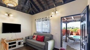 Een woonkamer met een grijze bank, een flatscreen televisie, een houten tv-meubel en uitzicht op een terras met een zwembad.