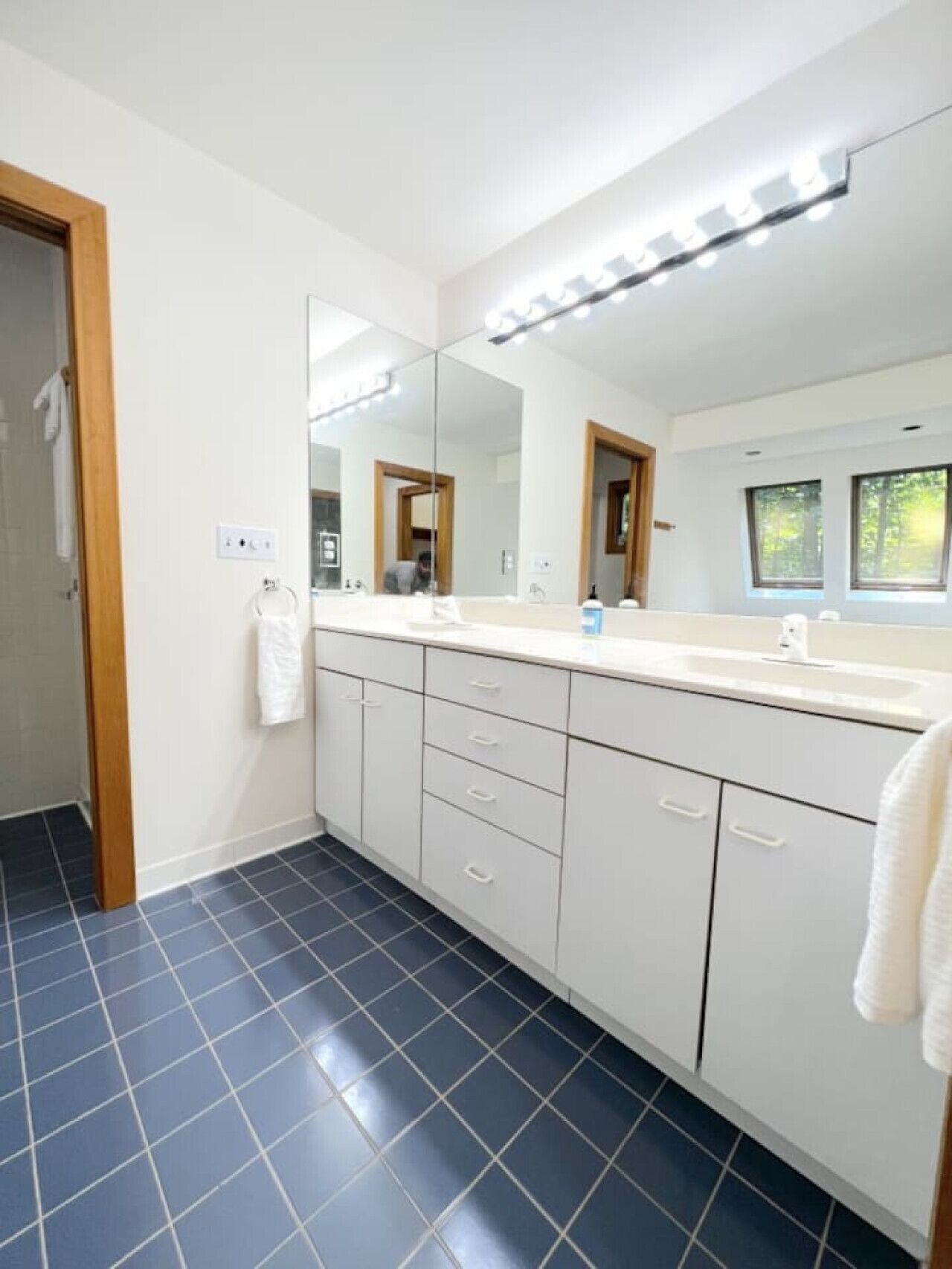 Un baño moderno con un espejo grande, armarios blancos y piso cubierto de azulejos azules.