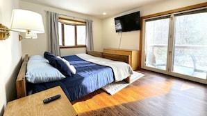 A bedroom with a bed, a TV, a window, and a wooden floor. - Stratton Mountain Home - Hot Tub, Fire Pit & Game Loft (Jamaica)