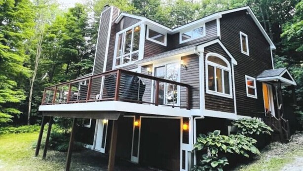 A two-story house with a balcony and a deck, surrounded by trees. - Stratton Mountain Home - Hot Tub, Fire Pit & Game Loft (Jamaica)