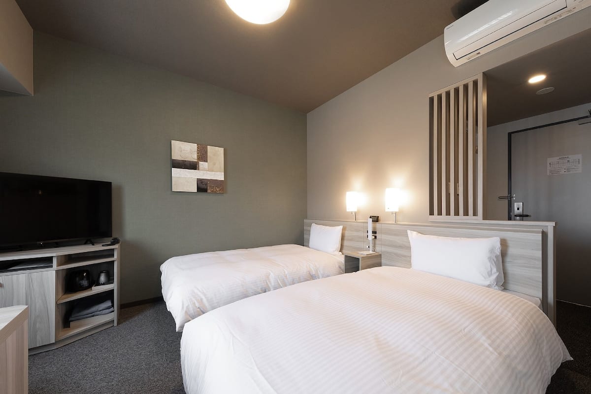 A hotel room with two beds, a TV, a wall-mounted artwork, and a ceiling fan.