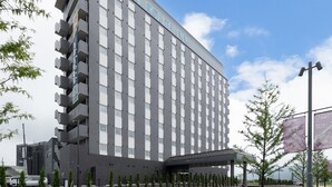 Un hotel moderno con fachada plana, varios balcones y una zona de entrada cubierta.