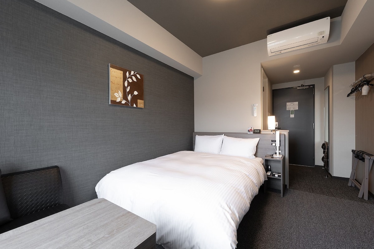 A hotel room with a bed, bedside table, and an air conditioning unit.