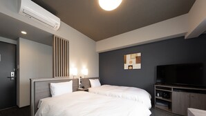 Habitación de hotel con dos camas, un televisor de pantalla plana, un minibar y aire acondicionado instalado en la pared.