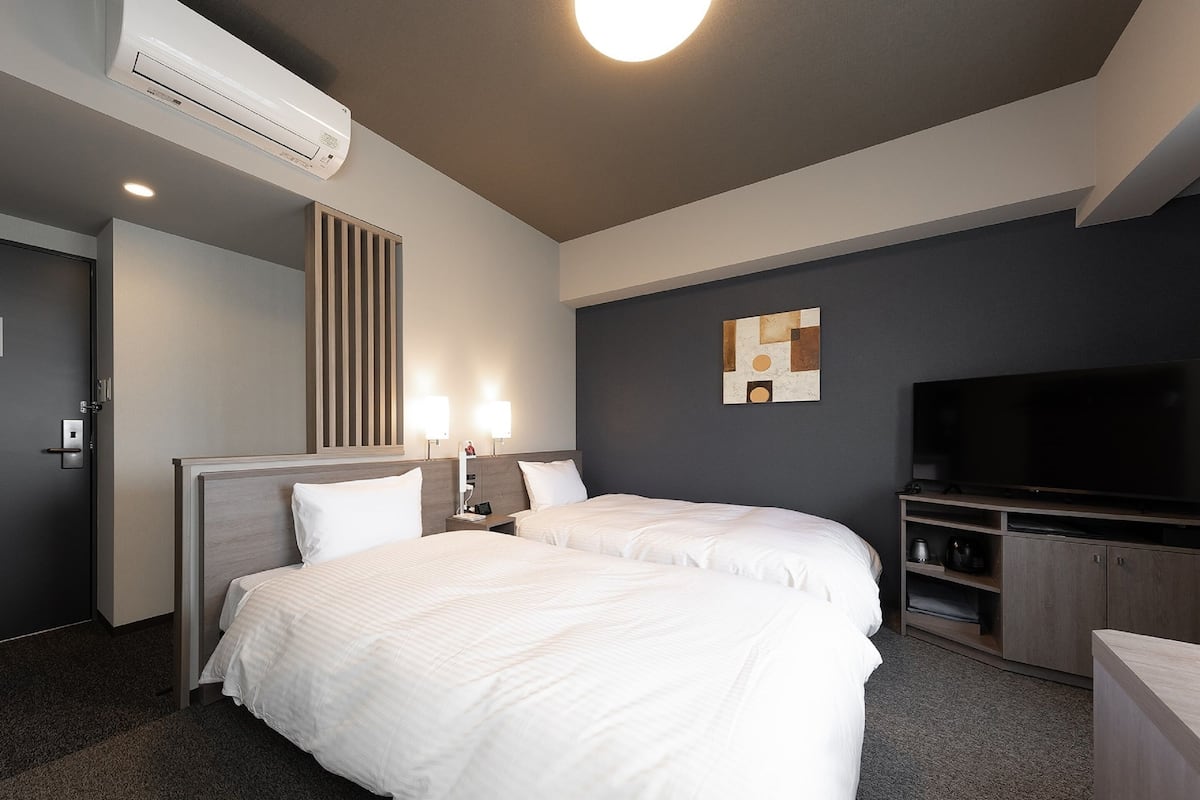 A hotel room with two beds, a flat-screen TV, a minibar, and a wall-mounted air conditioner.
