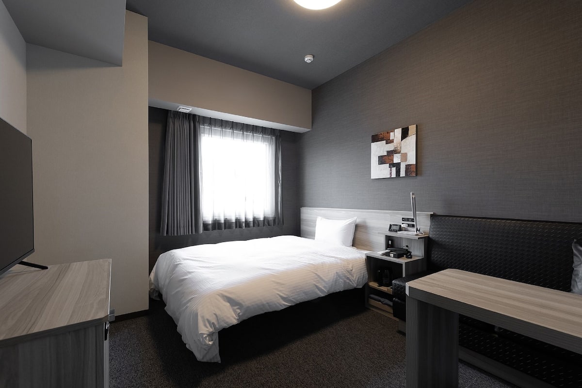 A modern hotel room with a large bed, bedside table, and a TV.
