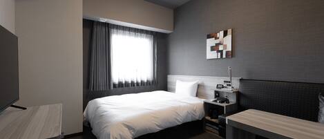 A modern hotel room with a large bed, bedside table, and a TV.