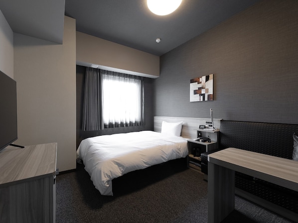 A modern hotel room with a large bed, bedside table, and a TV.