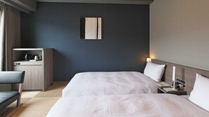 Camera d'albergo con due letti, una scrivania, una sedia, un comodino e un'opera d'arte appesa al muro.