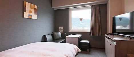 A hotel room with a bed, a desk, a TV, and a window with a view of the mountains.