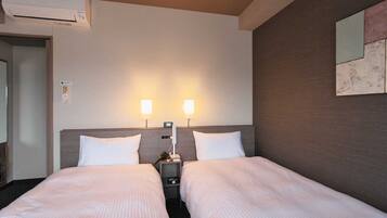 A hotel room with two beds, a wall-mounted air conditioner, bedside lamps, and a small table with a phone.