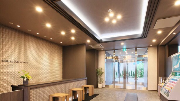 Zona reception di un hotel con parete in mattoni, scrivania in legno e area relax con panche.