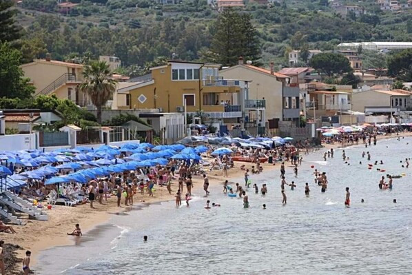 Ein überfüllter Strand mit vielen Sonnenschirmen und Menschen, die das Wasser genießen.