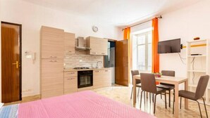 A compact hotel room with a kitchenette, a dining area, and a bed with a pink blanket. - Antonella House 1 (Trabia)