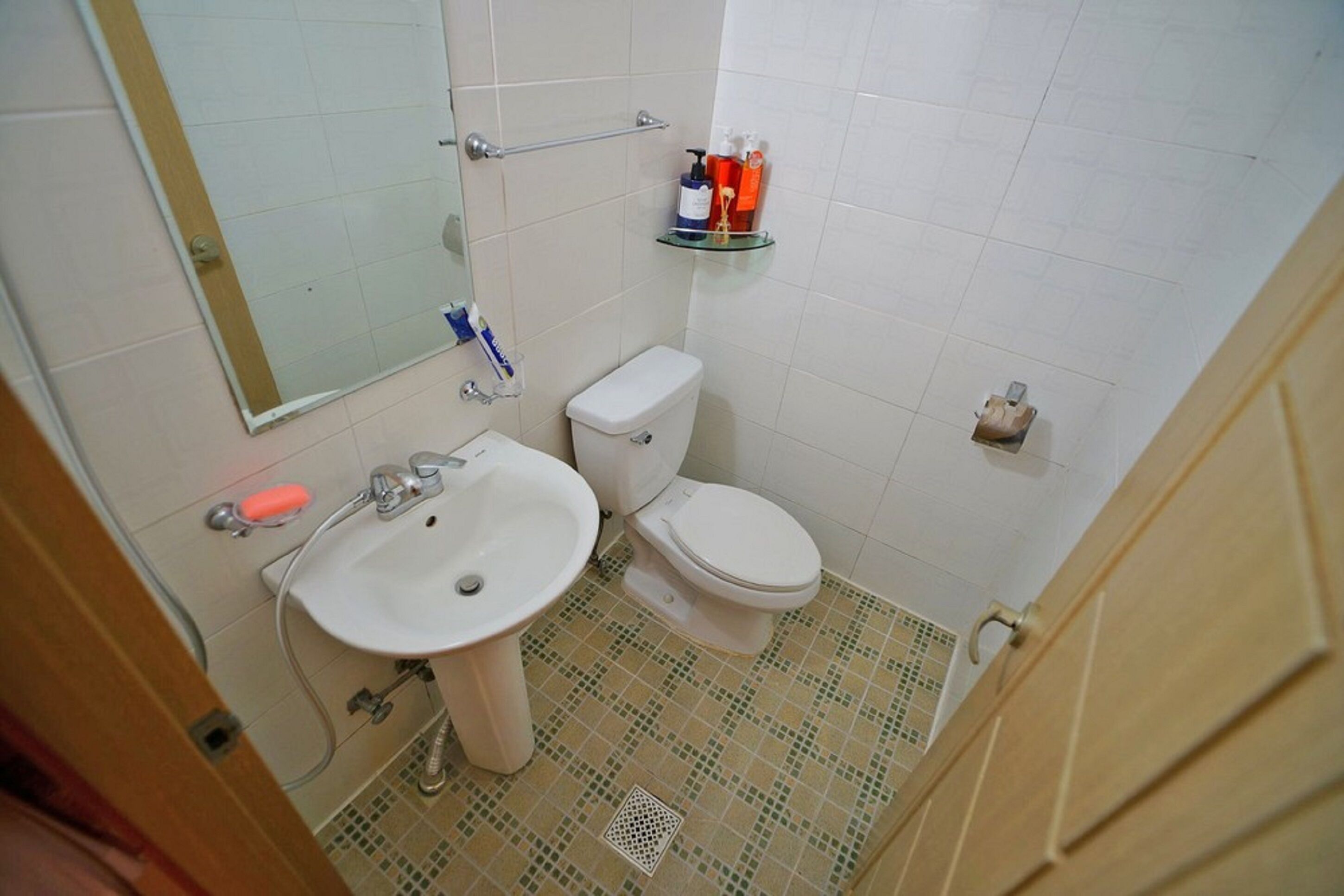 A small bathroom with a white sink, toilet, and a glass shelf with toiletries.