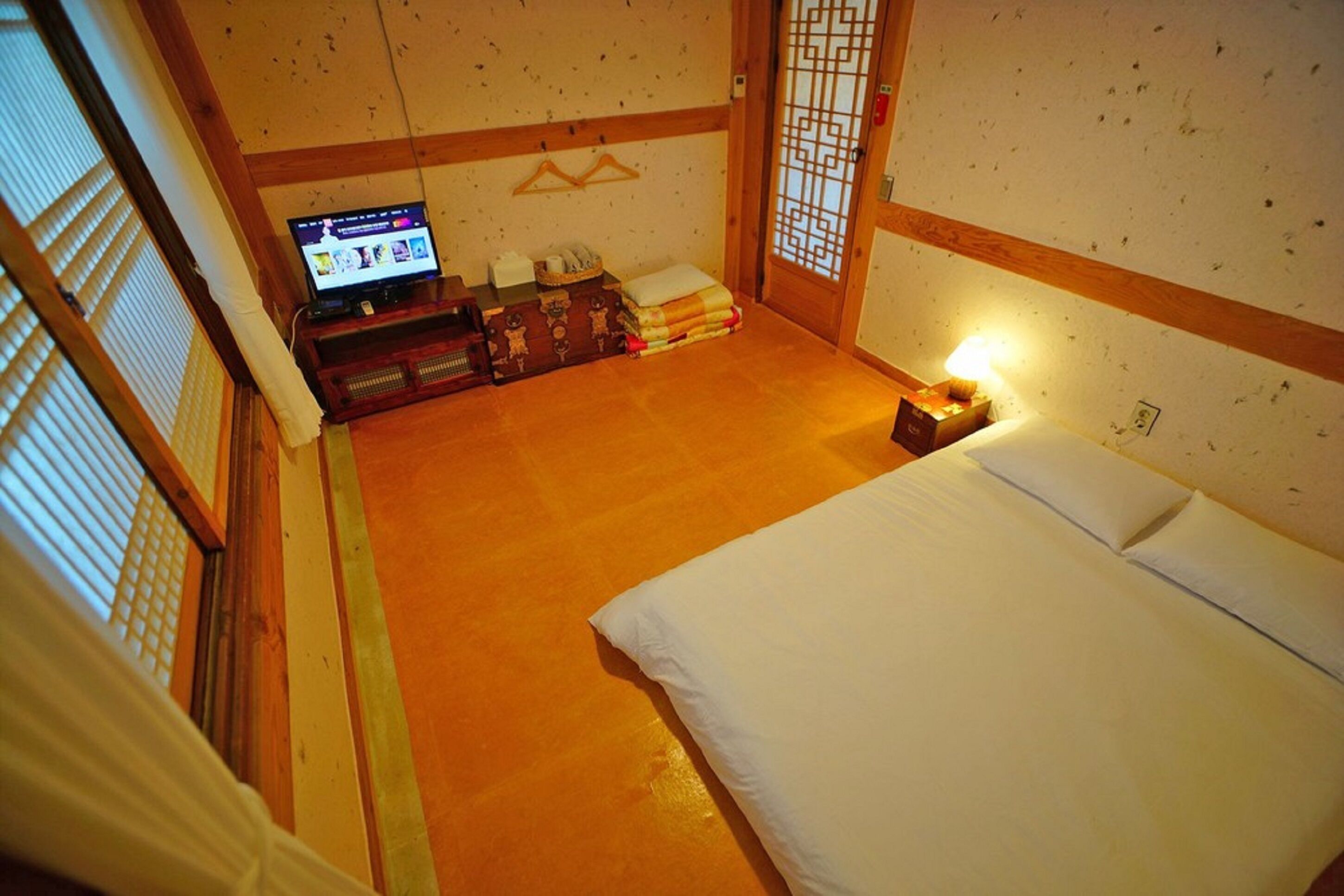 Een traditionele Japanse kamer met tatami vloer, een bed met witte beddengoed, een televisie op een lage tafel en een schuifdeur met een geometrisch patroon.