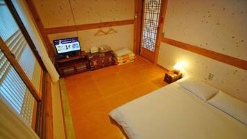 Een traditionele Japanse kamer met tatami vloer, een bed met witte beddengoed, een televisie op een lage tafel en een schuifdeur met een geometrisch patroon.
