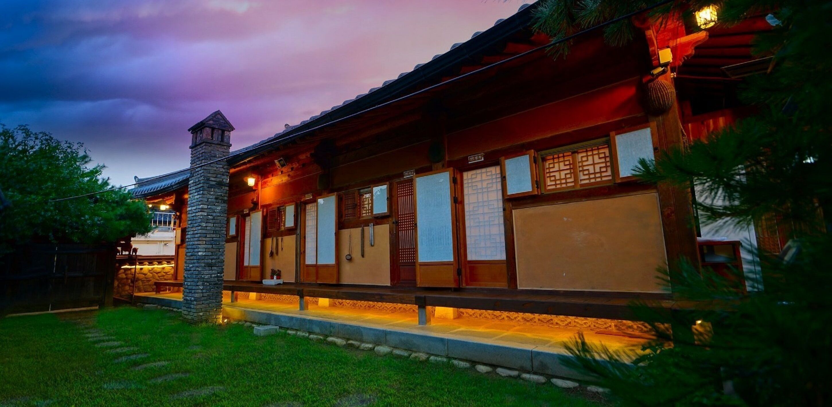 A traditional wooden house with a stone chimney, a wooden porch, and a well-maintained lawn.