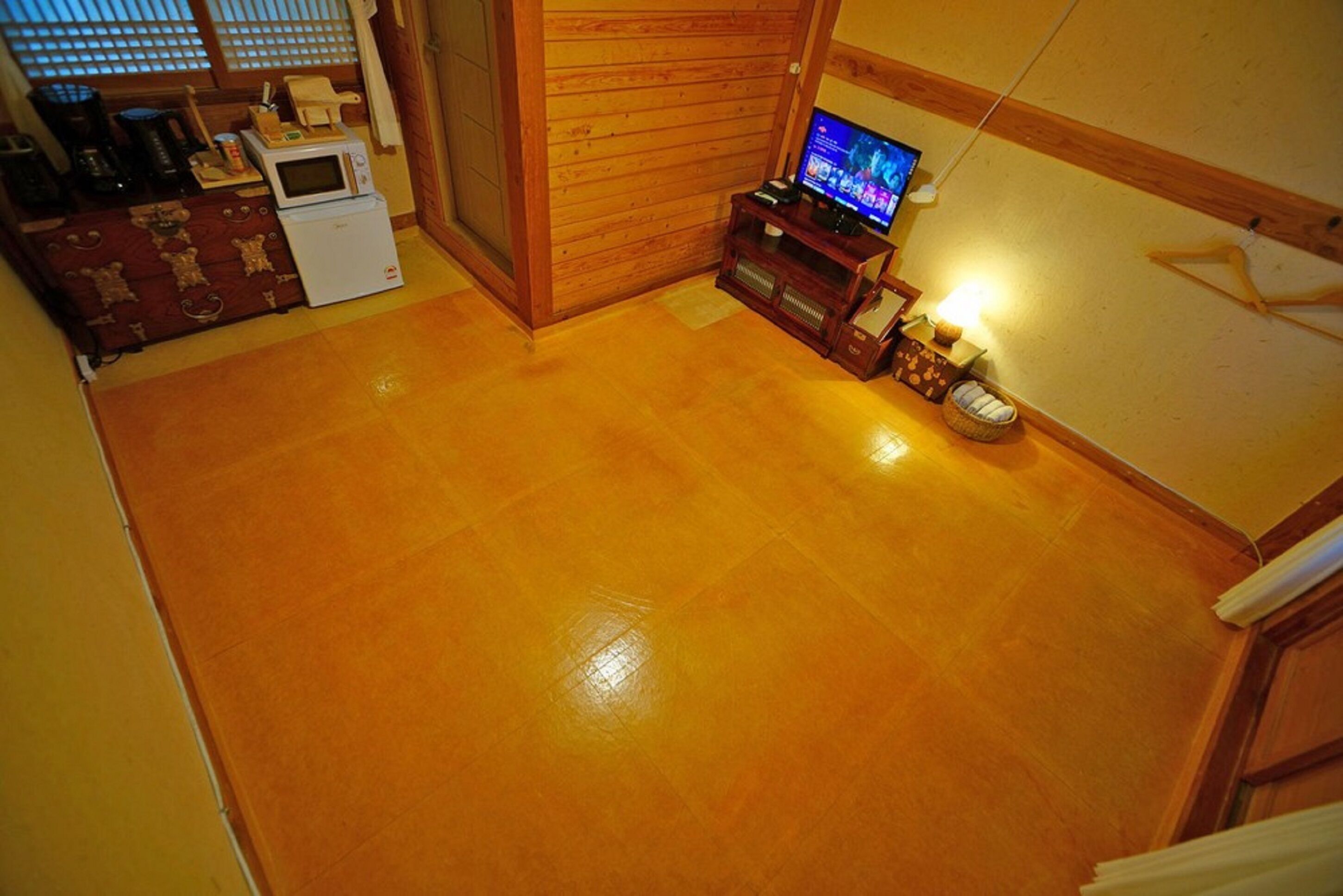 A compact living space with a wooden floor, a television on a wooden stand, a microwave, and a small refrigerator.